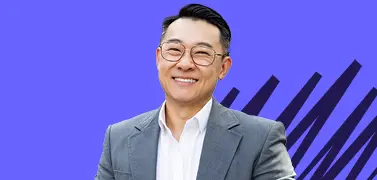 A young man in tuxedos smiling on a blue background.