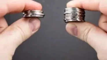 Twee handen houden verschillende stapels munten vast.