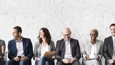 A group of people in business attire sitting against a brick wall.
