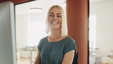 Vrouw die lacht achter een computerscherm in een kantooromgeving.