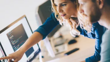 Collega's werken samen op een computer, wijzend naar het scherm.