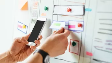 A person arranging notes on a whiteboard while holding a smartphone.