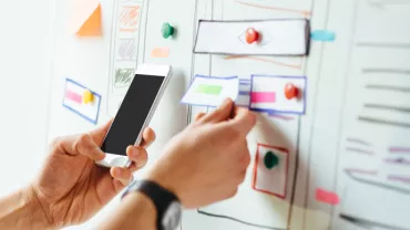 Iemand plaatst een briefje op een whiteboard met een smartphone in de hand.