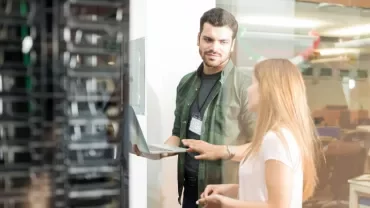 Two people discussing and using a laptop in a server room.