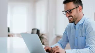 Persoon die lacht terwijl hij op een laptop typt in een kantooromgeving