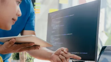 Twee mensen werken op een computer, één wijst naar het scherm.