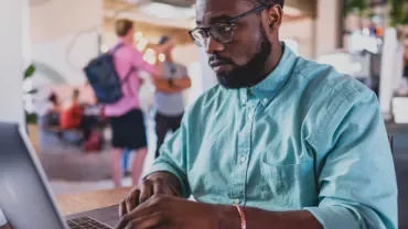 Person working on a laptop in a cafe with others in the background.