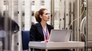 Person working on a laptop in a server room.