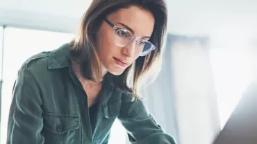 Person focused on a laptop screen in a bright room.