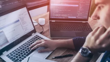 Persoon werkt aan computercode op laptops.