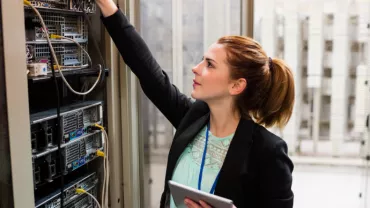 Persoon werkt in een serverruimte, bezig met kabels en apparatuur.