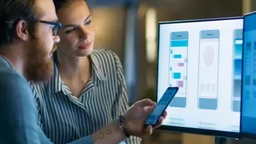 Two people collaborating on a mobile app design displayed on a computer screen.