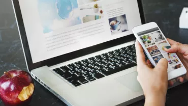 Iemand gebruikt een smartphone met een laptop op tafel.
