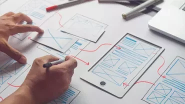 Person designing a mobile layout with wireframes and a laptop.