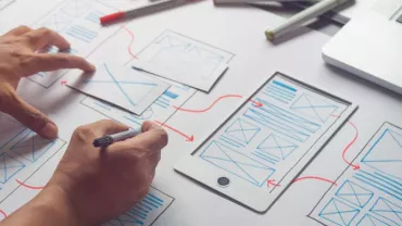 Ontwerper werkt aan mobiel ontwerp met wireframes en laptop.