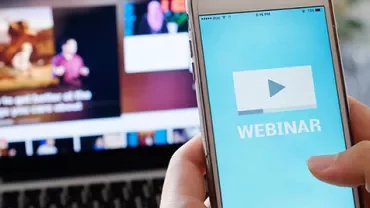 Person holding phone with webinar screen, laptop in background.
