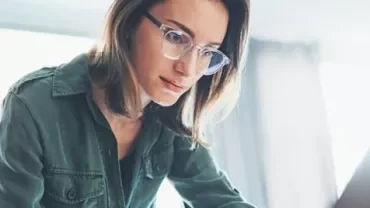 Person with glasses working intently on a laptop