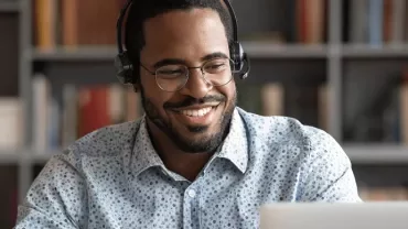 Persoon met een headset voor laptop, omringd door boeken in een kast.