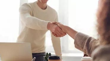 Twee mensen schudden elkaar de hand bij een bureau.