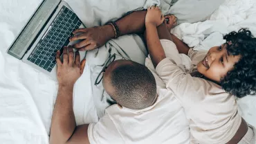 Two people relaxing on a bed with a laptop.