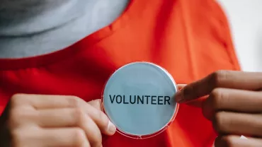 Persoon met vrijwilliger badge en oranje schort.