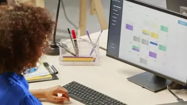 Persoon werkt aan bureau met computerscherm en agenda.