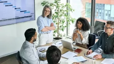 Coworkers in a meeting room discussing a presentation on screen.