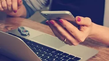 Person using a smartphone and laptop at a desk.