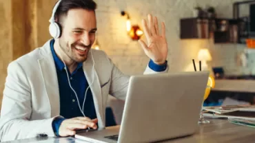 Man met koptelefoon zwaait naar laptop in café.