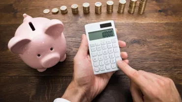 Person using a calculator near a piggy bank and stacks of coins.