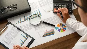Person analyzing charts and using a calculator at a desk.