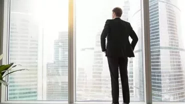 Person standing in an office, looking out at the city skyline.