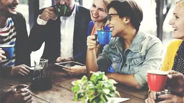 Group of people having coffee together and smiling around a table.