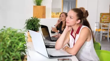 Two people working on laptops in a bright office space.