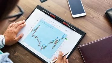 Person viewing business chart on tablet next to phone and notebook.
