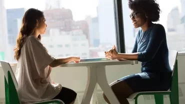 Two people talking at a table with a city view.