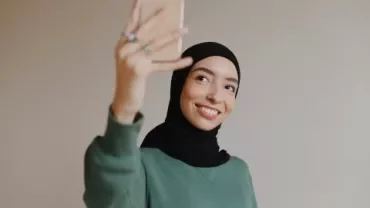 Persoon maakt een selfie met een smartphone, glimlachend.