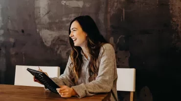 Person laughing and writing in a notebook at a table.