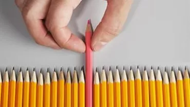 Hand picking a pink pencil from a line of yellow pencils.