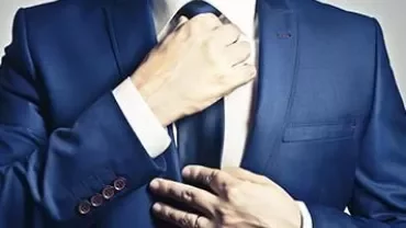 Person adjusting a tie on a blue suit.