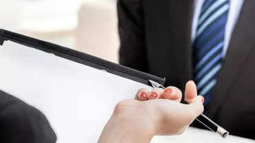 Een persoon geeft een pen en documenten aan een ander tijdens een gesprek.
