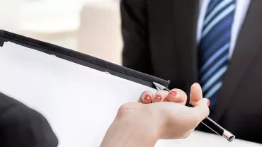 Een persoon geeft een pen en documenten aan een ander tijdens een gesprek.