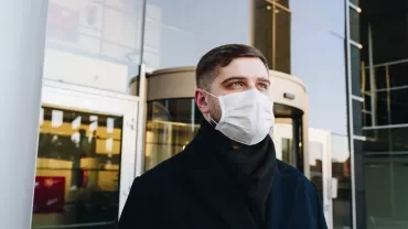 Person wearing a mask outside glass building