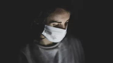 Person wearing a mask, looking down in the dark.
