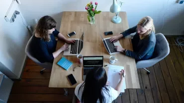 Three people collaborating at a table with laptops and coffee.