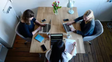 Three people collaborating at a table with laptops and coffee.