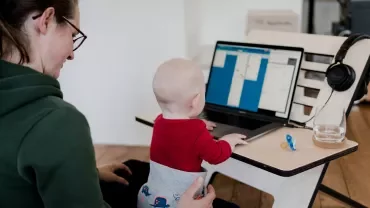 Volwassene met kind op schoot, kijkend naar een laptop.
