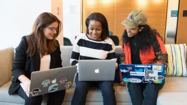 Three people collaborating with laptops on a couch.