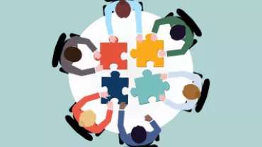 Group of people collaborating on puzzle pieces at a table.