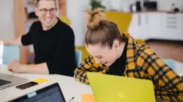 Twee mensen lachen samen terwijl ze met laptops werken.